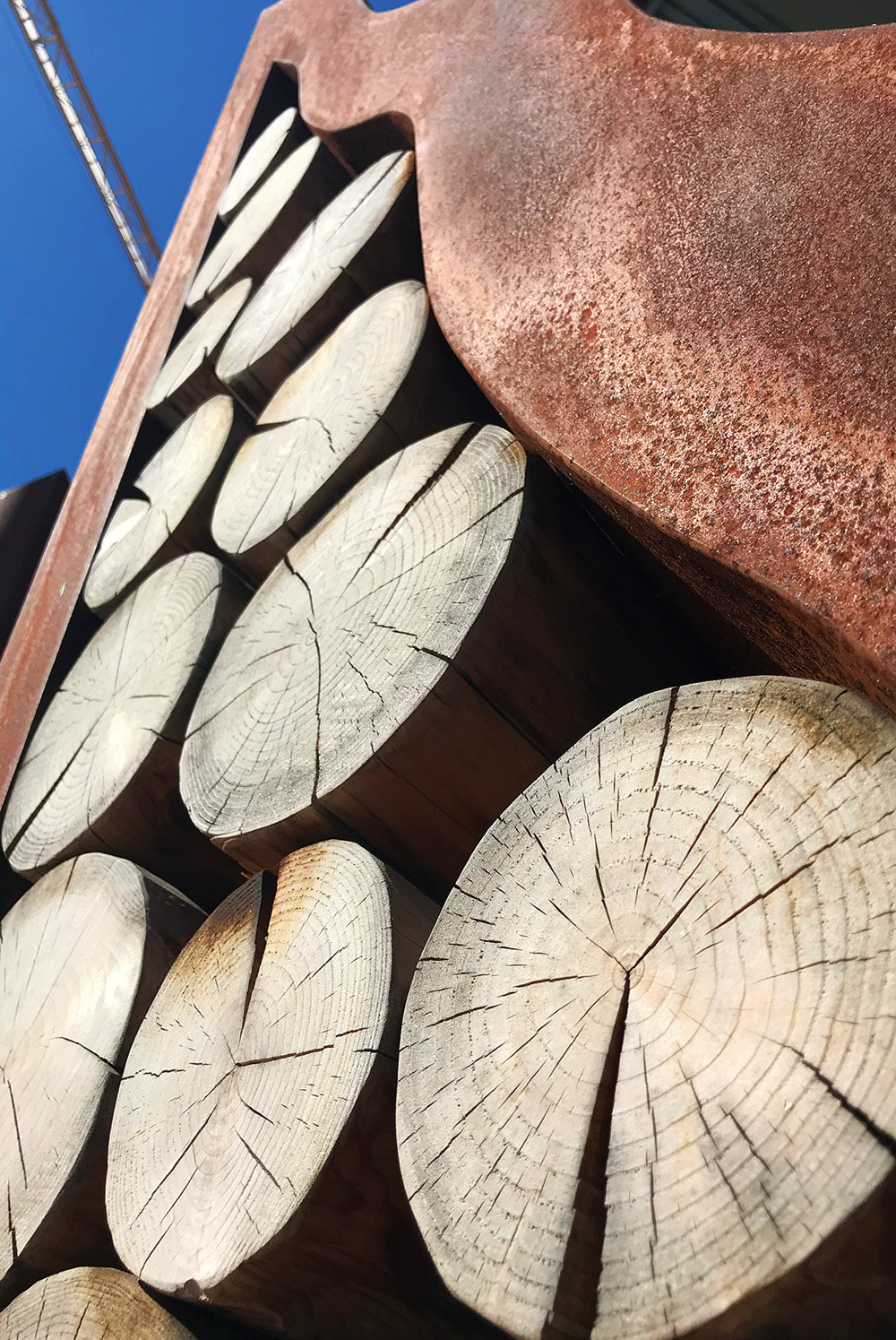 angle photo of a corten sculpture with cedar logs inserted into it