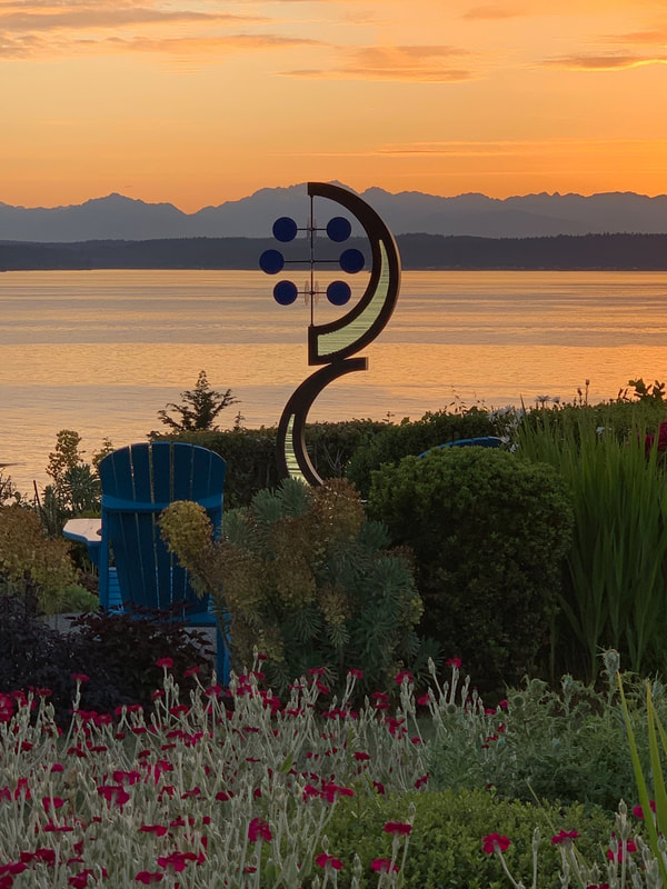 two half circle stacked on top of each other sculpture of bronze and glass with background of sea and mountians kinetic