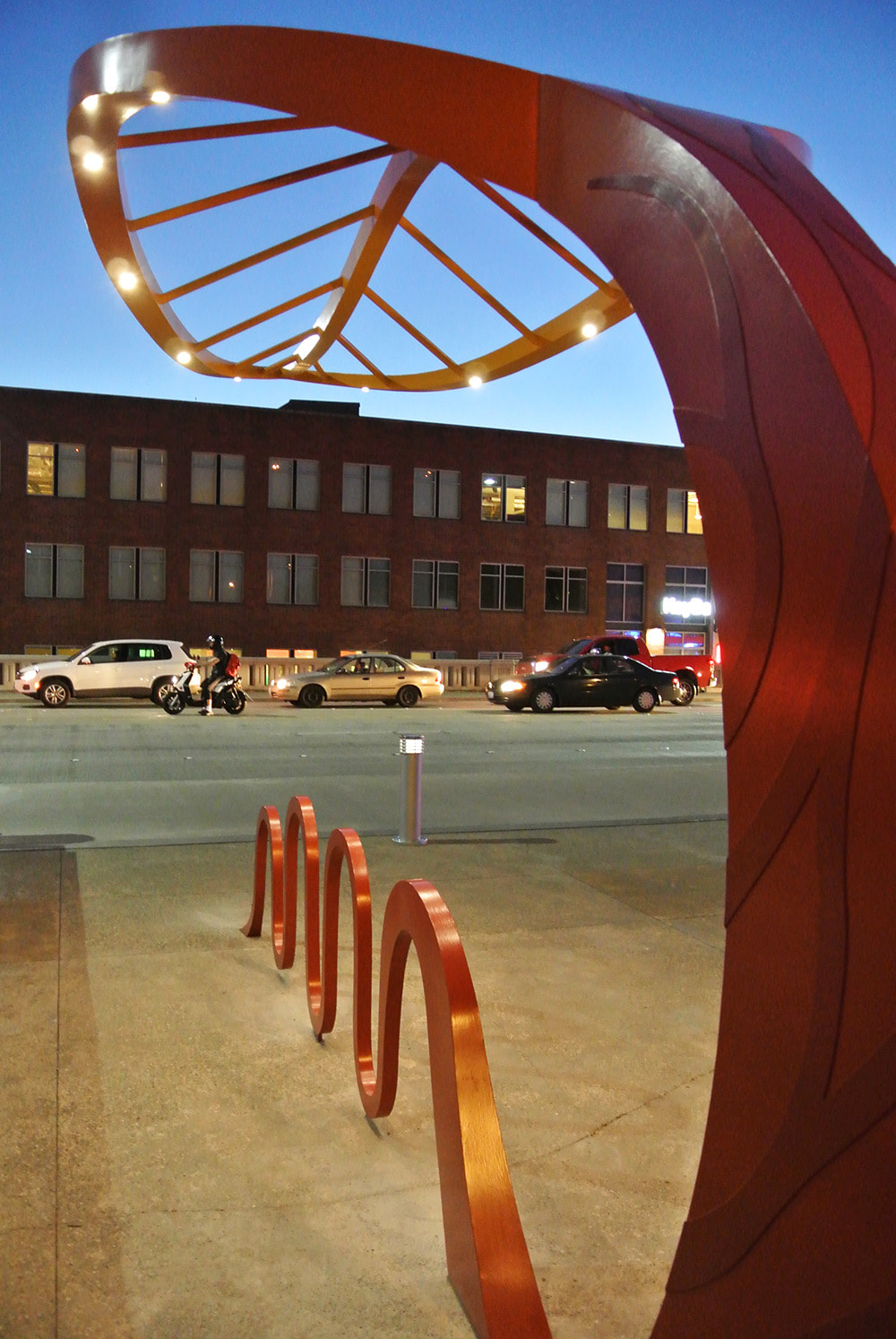 angle photo of a leaf sculpture with cars in the background at dusk